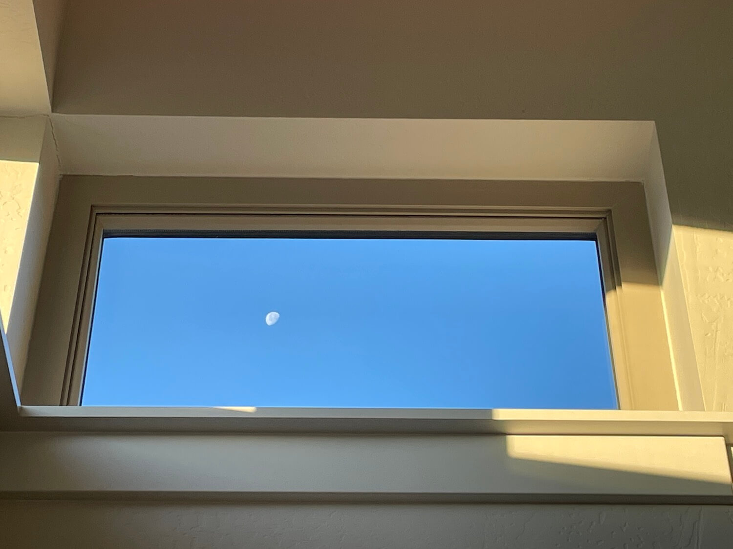 a view of the setting moon against a bright blue sky through a window that is framed with the sun around it