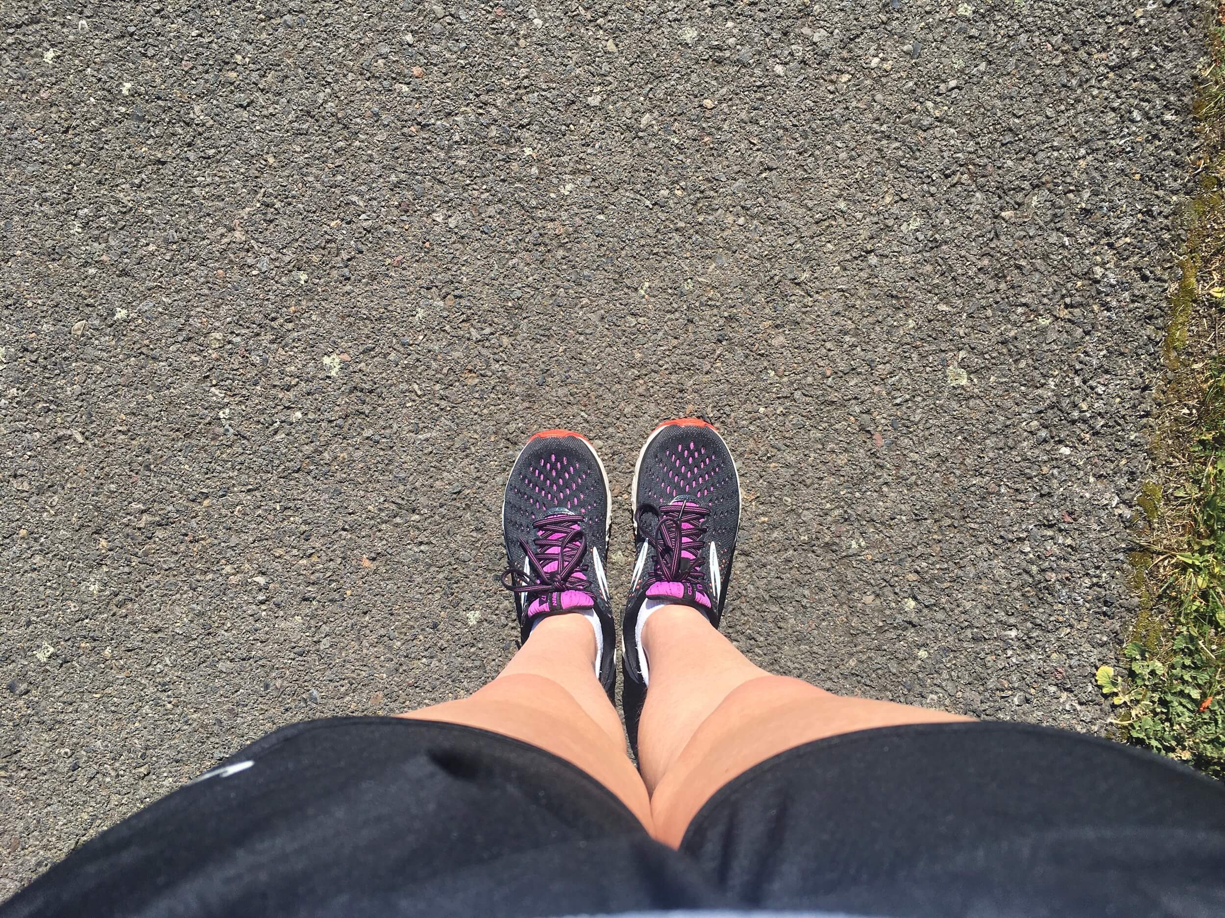 a photo of my legs in shorts with my feet in running shoes, on top of tar