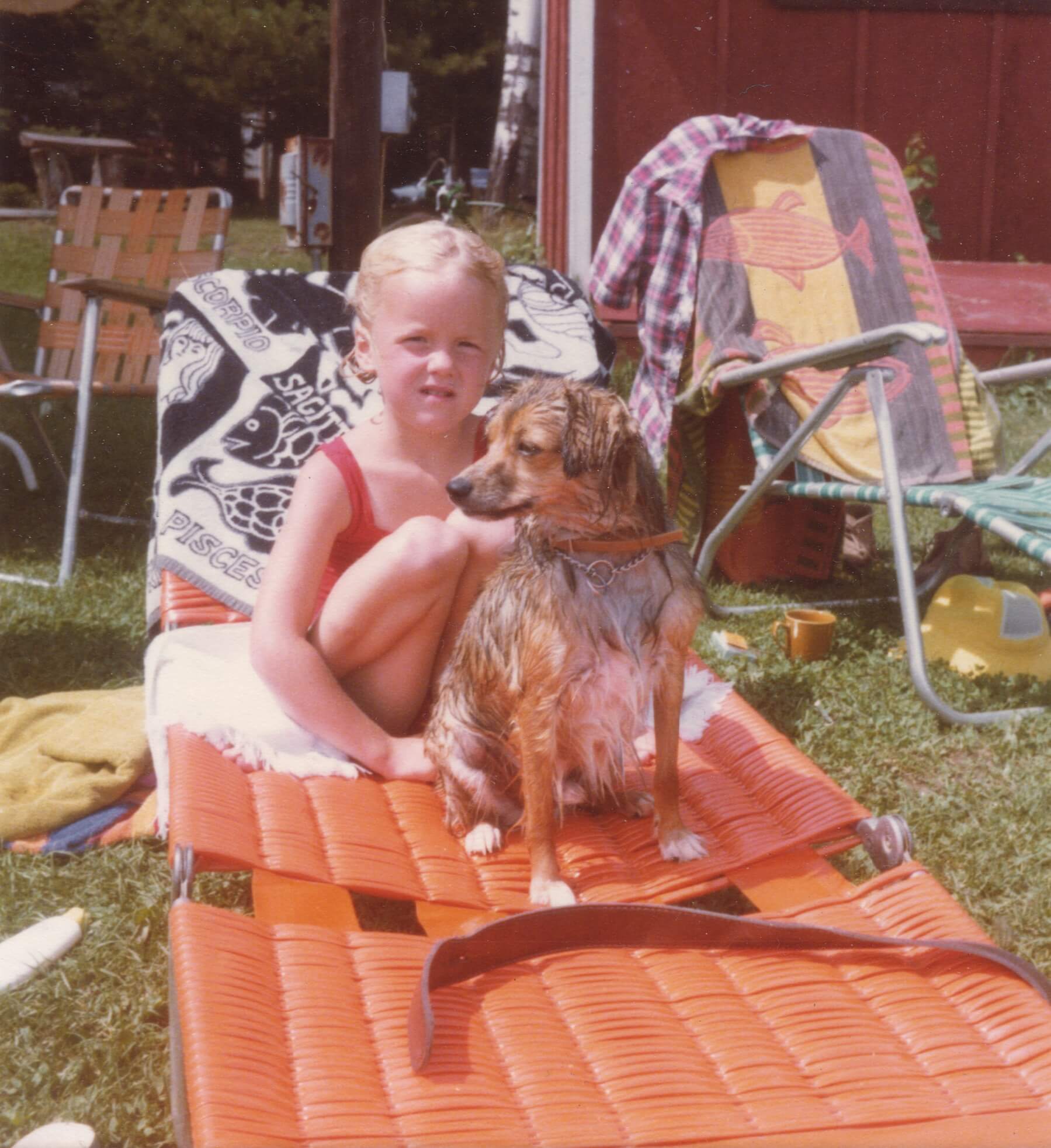 A young me, five years old, sitting on a lounge chair with towels strewn across the back of it, other lounge chairs are in the background, and a small, wet, dog sits in front of me, as I stare at the photographer with a hint of skepticism.